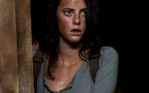 Twarz Kaji Scodelario, aktorki znanej z filmów i seriali, z przerażeniem w oczach, w ciemnym otoczeniu.