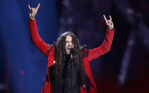 Michał Szpak na Eurowizji w czerwonej marynarce, z uniesionymi rękami i gestem rock'n'rolla.