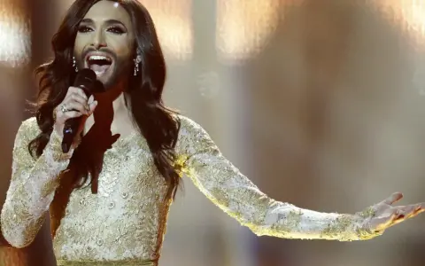 Conchita Wurst, zwyciężczyni Eurowizji, w złotej sukni z cekinami śpiewa na scenie.