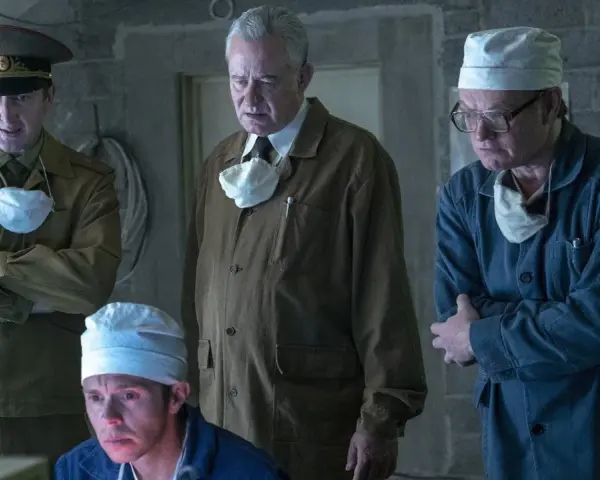 Mężczyźni w mundurach i fartuchach, w tym jeden w wojskowym, analizują coś na ekranie. Scena z serialu Czarnobyl Netflix.