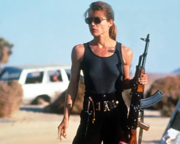 Linda Hamilton w roli Sary Connor, gotowa do walki w pustynnym krajobrazie. Jej ikoniczne role w filmach i serialach na zawsze zapisały się w historii kina.