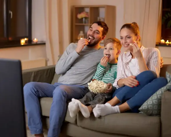 Rodzina ogląda filmy familijne, zajadając popcorn. Radość i wspólne chwile na kanapie.