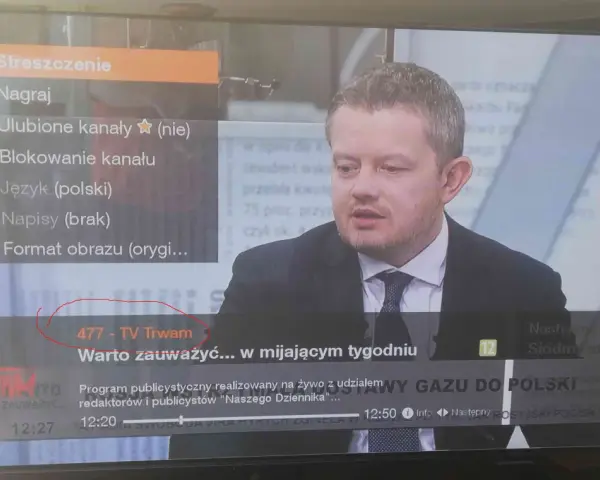 Mężczyzna w garniturze na ekranie telewizora, na którym widać menu z opcją "477 - TV Trwam".