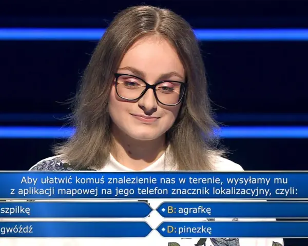 Młoda kobieta w okularach na tle niebieskich pasów, zastanawia się nad pytaniem z teleturnieju: "Aby ułatwić komuś znalezienie nas w terenie, wysyłamy mu z aplikacji mapowej na jego telefon znacznik lokalizacyjny, czyli: B: agrafkę".
