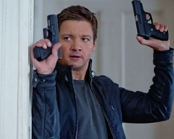 Jeremy Renner w akcji, jakiego znamy z jego filmów i seriali. W rękach trzyma dwa pistolety, gotowy do strzału.
