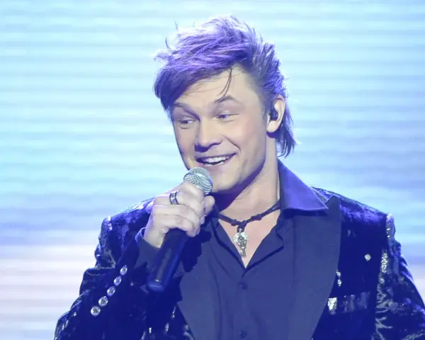 Jaka to melodia piosenkarze: przystojny mężczyzna z fioletowymi włosami śpiewa do mikrofonu w błyszczącej marynarce.