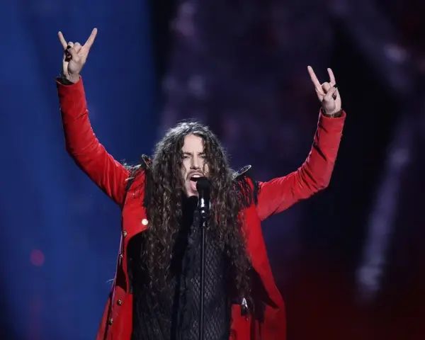 Michał Szpak na Eurowizji w czerwonej marynarce, z uniesionymi rękami i gestem rock'n'rolla.
