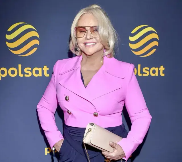 Kobieta w różowej marynarce i okularach, pozuje na tle logo Polsat. Może to być jedna z gwiazd serialu "Teściowie" w obsadzie.