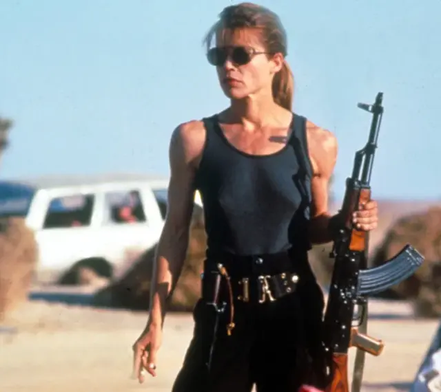 Linda Hamilton w roli Sary Connor, gotowa do walki w pustynnym krajobrazie. Jej ikoniczne role w filmach i serialach na zawsze zapisały się w historii kina.