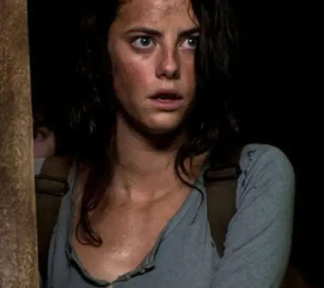 Twarz Kaji Scodelario, aktorki znanej z filmów i seriali, z przerażeniem w oczach, w ciemnym otoczeniu.