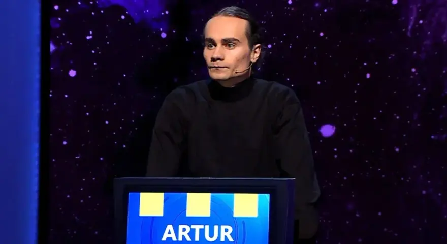 Artur, który wygrał jeden z dziesięciu, stoi na scenie w czarnym golfie.