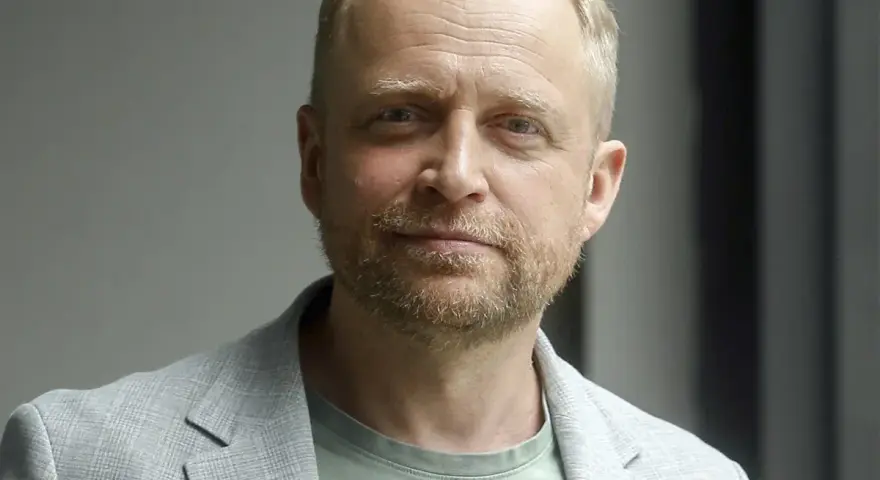 Piotr Adamczyk, znany z wielu filmów, seriali i programów, w jasnej marynarce i zielonej koszulce.