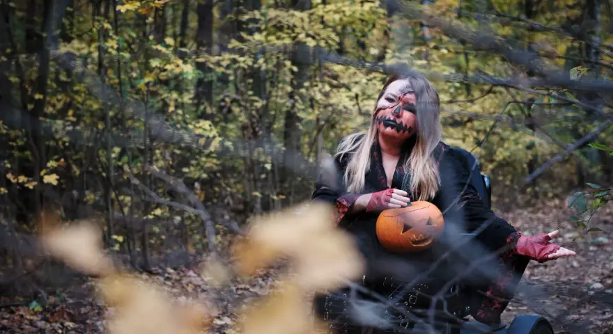 Kobieta w makijażu jack-o'-lantern trzyma dynię, gotowa na noc pełną **horrorów Netflix** w jesiennym lesie.