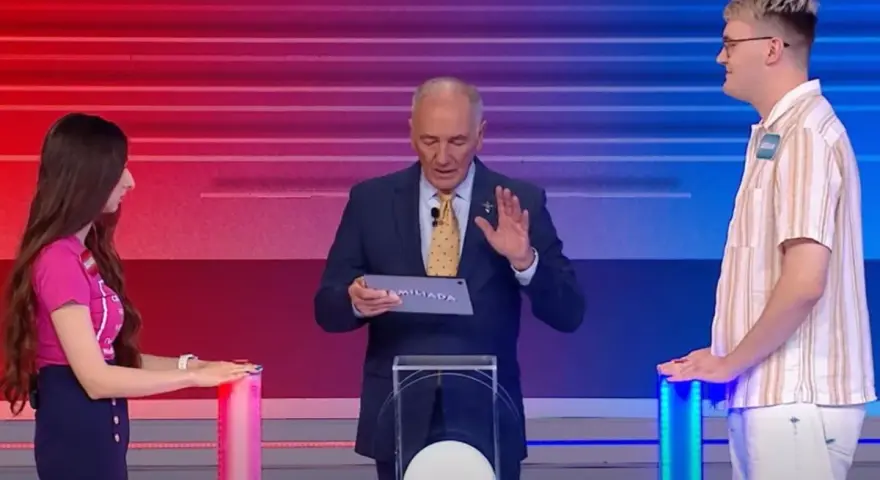 Na planie Familiady, prowadzący trzyma tablet z napisem "FAMILIADA". Po bokach stoją uczestnicy.