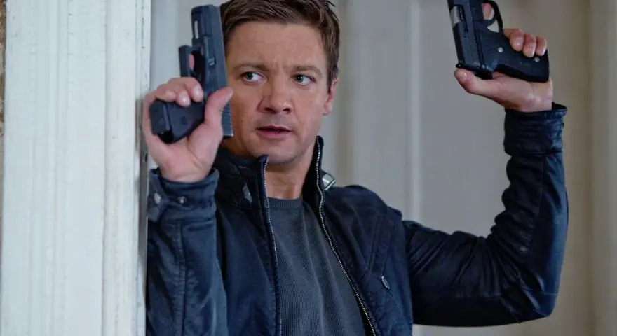 Jeremy Renner w akcji, jakiego znamy z jego filmów i seriali. W rękach trzyma dwa pistolety, gotowy do strzału.