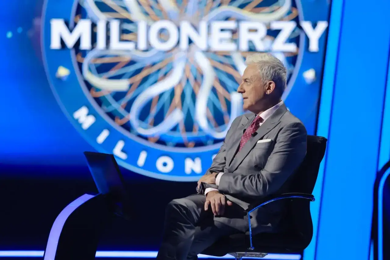Mężczyzna w garniturze siedzi na krześle przed logo
