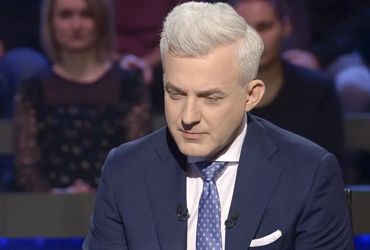 Prowadzący w garniturze, jak działa telefon do przyjaciela w Milionerach. Widownia w tle.