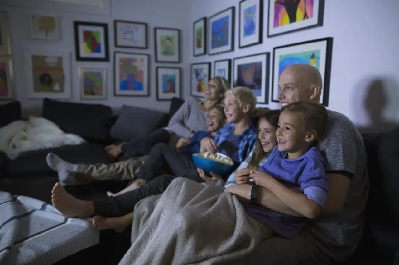 Rodzina śmieje się podczas oglądania filmów familijnych na kanapie, jedząc popcorn.
