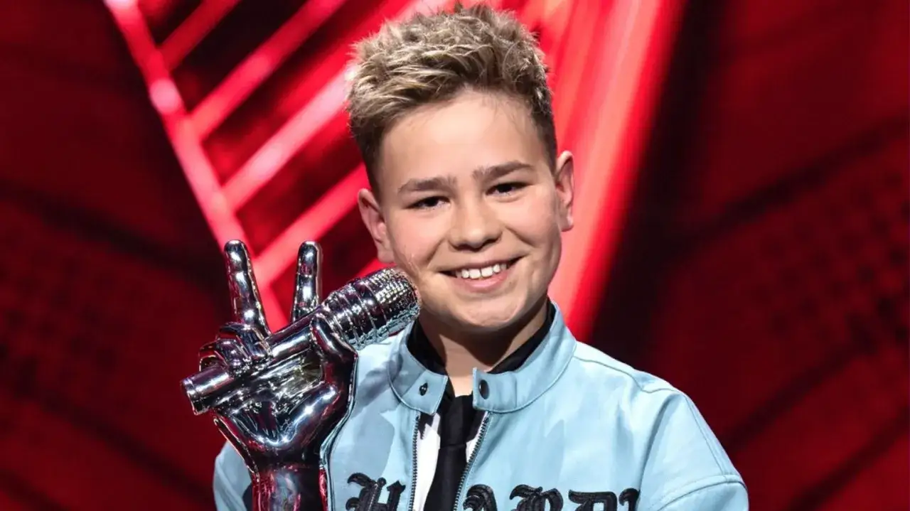 Szczęśliwy chłopiec z mikrofonem, zwycięzca The Voice Kids, z dumą prezentuje swój sukces.