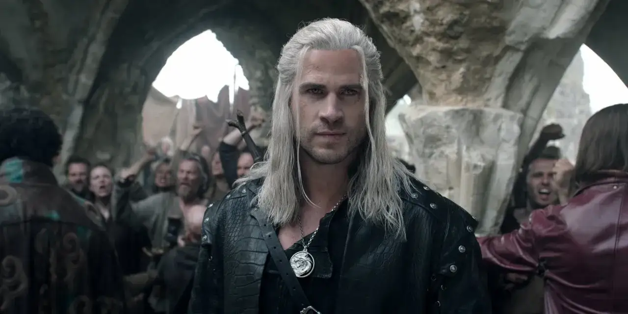 Geralt z Rivii, w czarnej skórzanej kurtce, stoi przed wzburzonym tłumem. To scena z serialu Wiedźmin, która pokazuje jego kolejność w walce o przetrwanie.