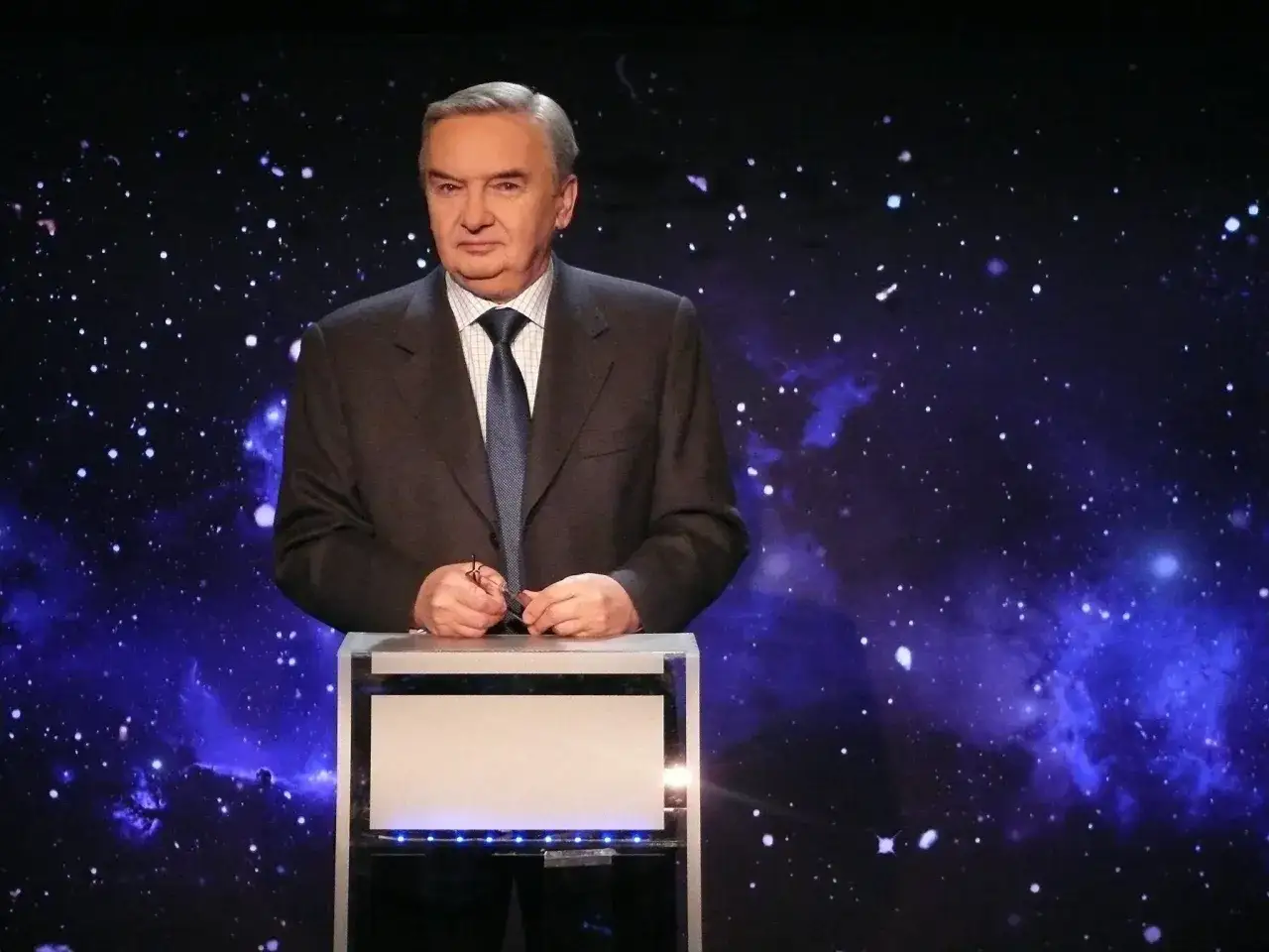 Mężczyzna w garniturze, jakby od kiedy jest jeden z dziesięciu, stoi na tle kosmicznego nieba.