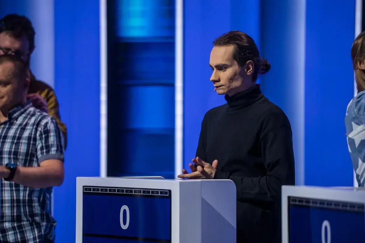 Młody mężczyzna w czarnym golfie, jeden z dziesięciu, czeka na swoją kolej w wielkim finale.