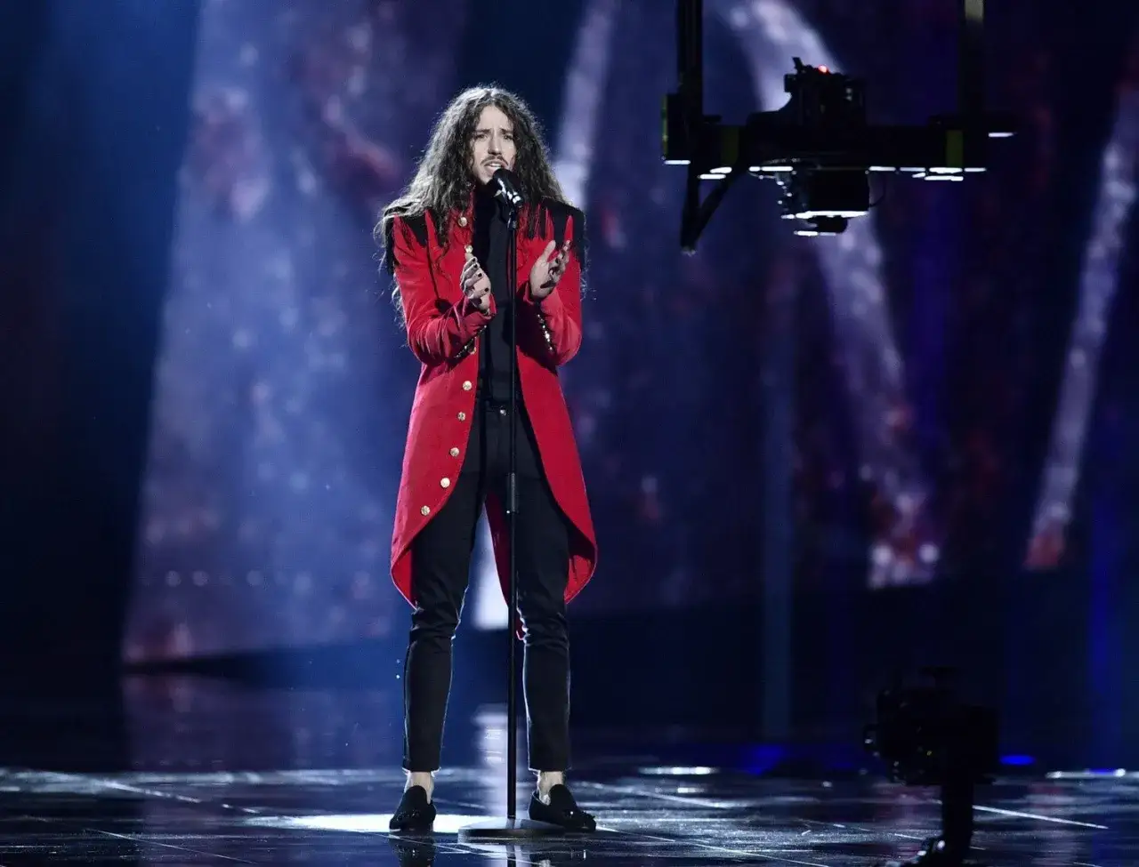 Michał Szpak na Eurowizji w czerwonym fraku, z charakterystyczną fryzurą, śpiewa na scenie.