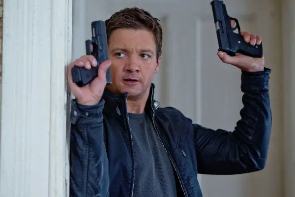 Jeremy Renner w akcji, jakiego znamy z jego filmów i seriali. W rękach trzyma dwa pistolety, gotowy do strzału.
