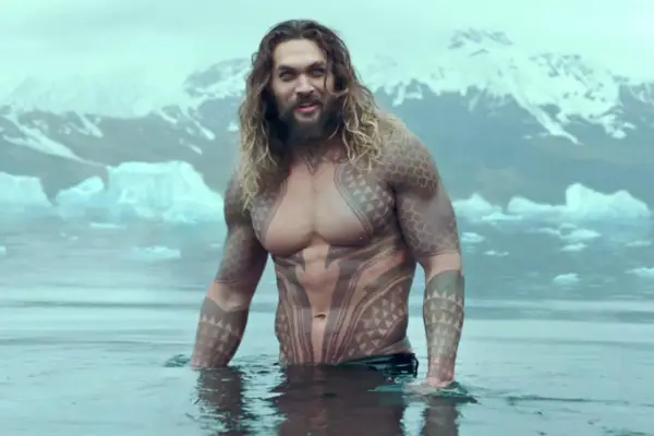 Jason Momoa w wodzie, z tatuażami, jak w filmach i serialach. W tle góry i lód.