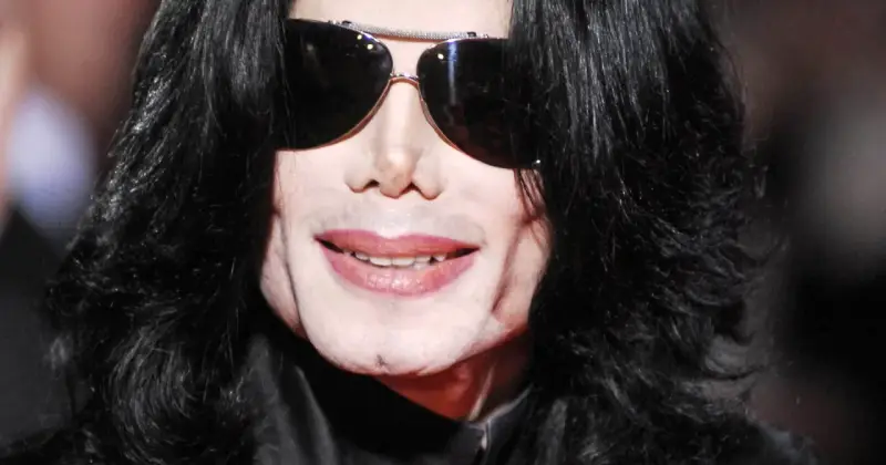 Michael Jackson w okularach przeciwsłonecznych i czarnych włosach. Jego uśmiech i twarz budzą pytania, jak zmarł Michael Jackson.