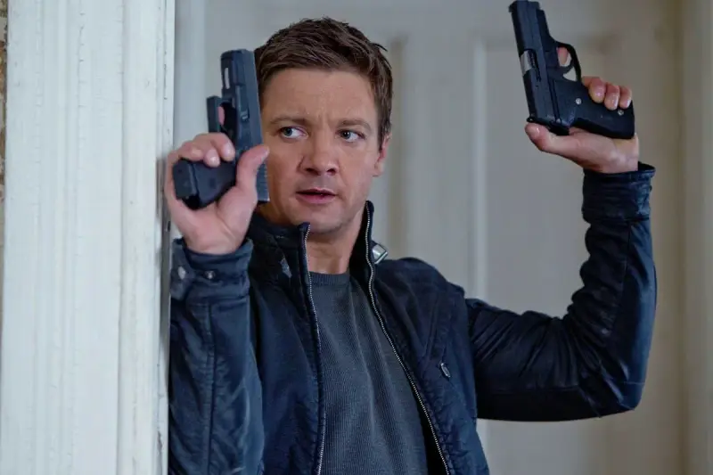Jeremy Renner w akcji, jakiego znamy z jego filmów i seriali. W rękach trzyma dwa pistolety, gotowy do strzału.