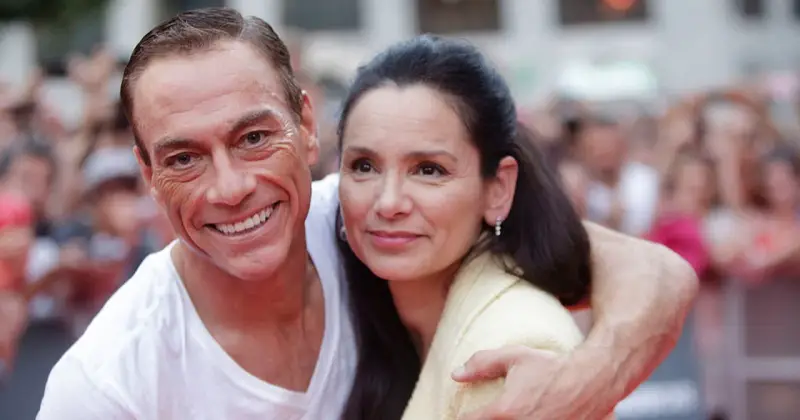 Jean-Claude Van Damme z uśmiechem obejmuje swoją żonę, Gladys Portugues, na tle tłumu.